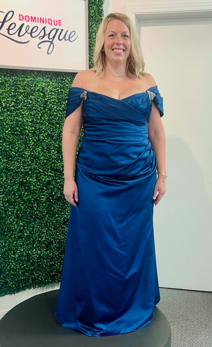 Woman in a dark blue dress in front of leaf background.