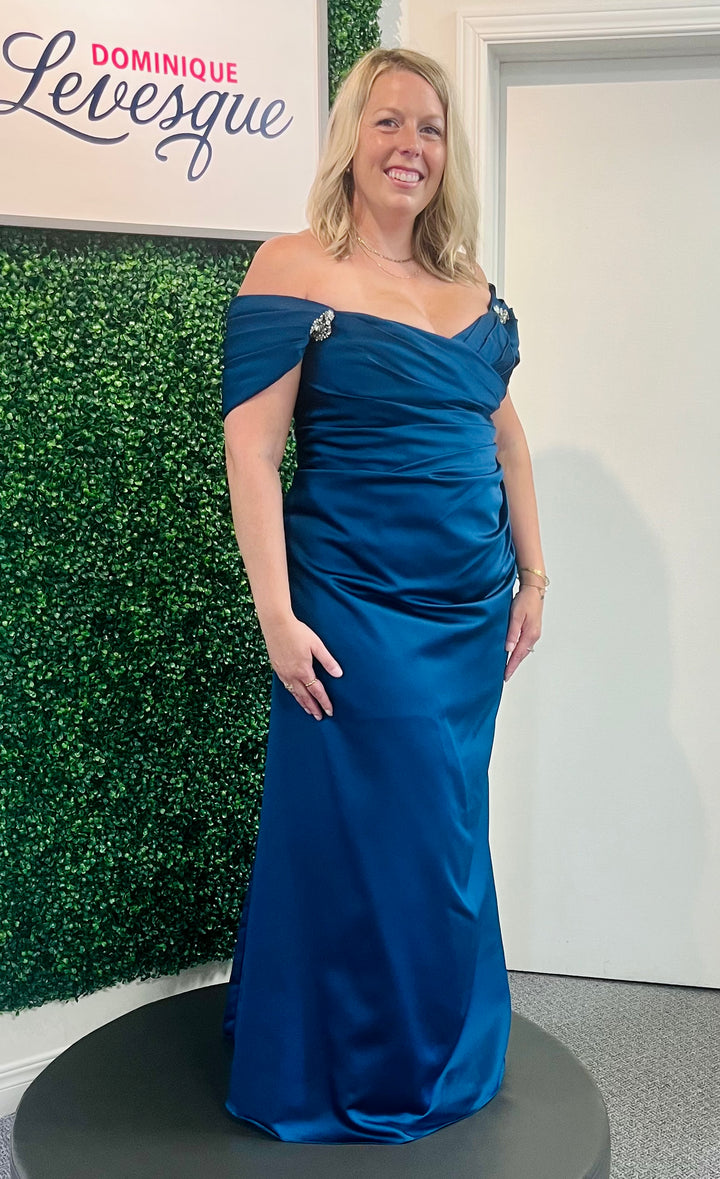 Woman in a dark blue dress in front of leaf background.
