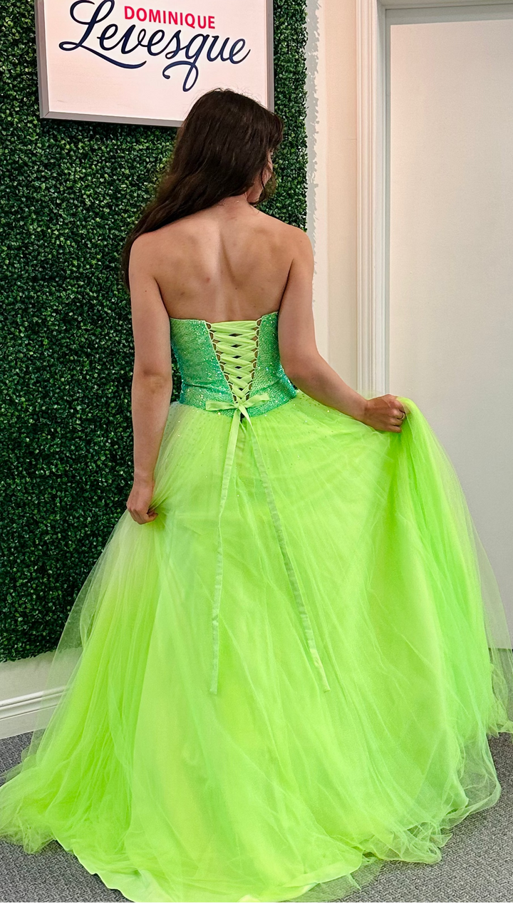 Woman in a bright green strapless gown standing against a wall.