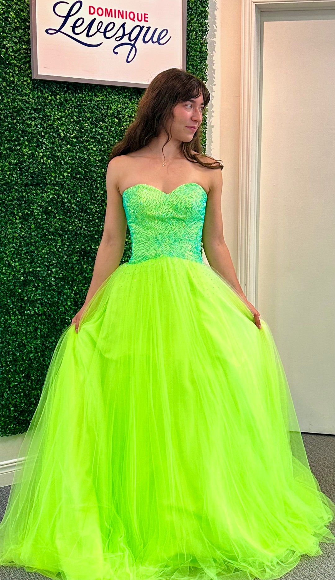 Woman wearing a lime strapless gown in an indoor setting with a green wall.