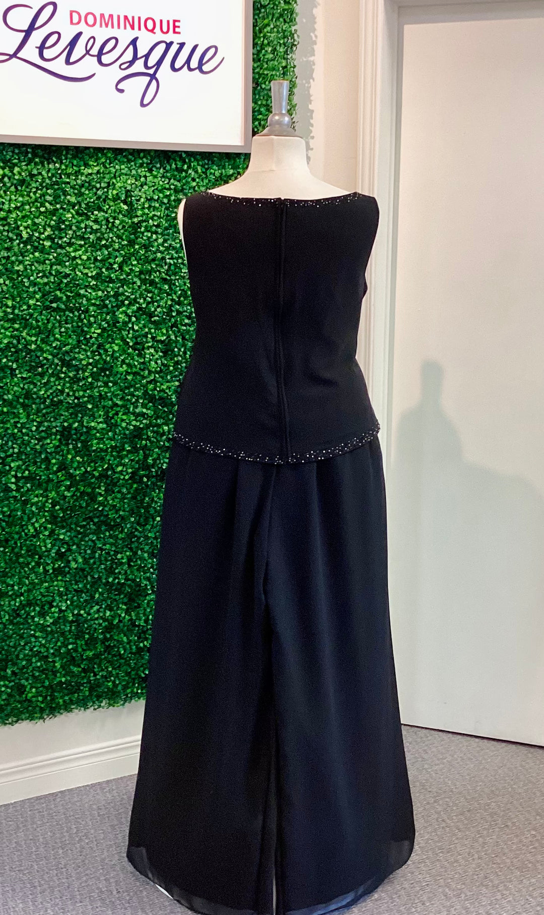 Black pants and top  on a mannequin against a green wall with &