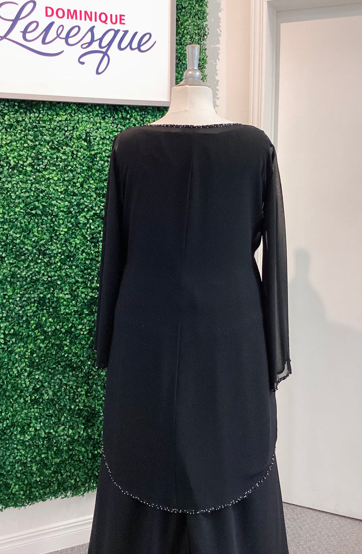 Black pants and top with vest on a mannequin against a green wall with &