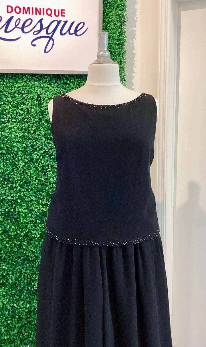 Black pants and top on a mannequin against a green wall with &