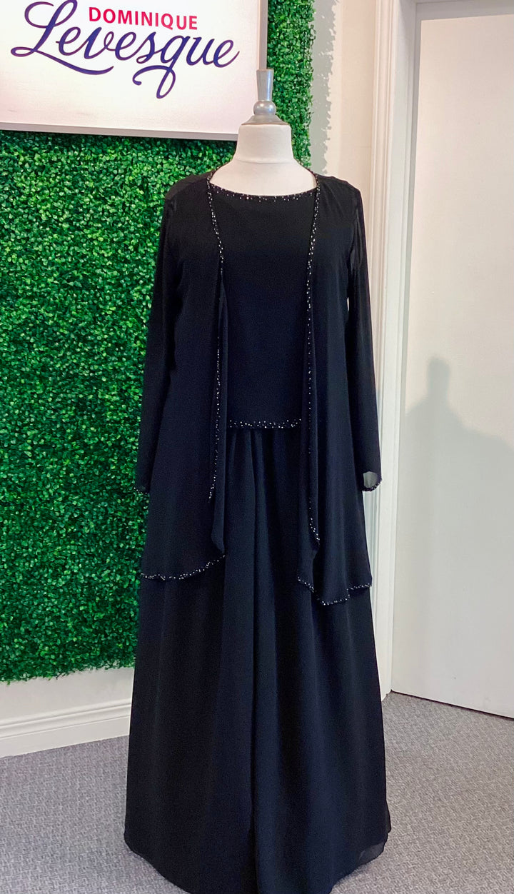Black pants and top with vest on a mannequin against a green wall with &