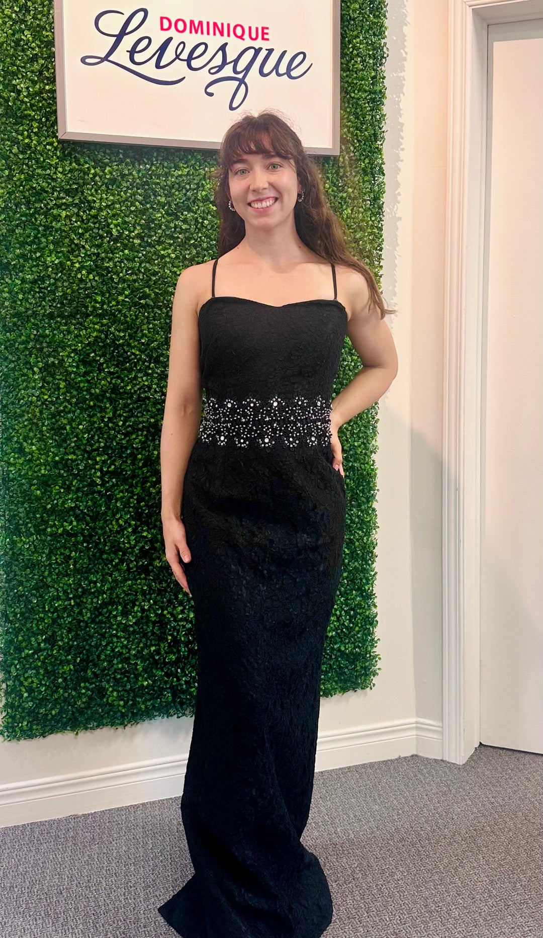 Woman in a black evening gown standing in front of a green wall with a sign above.