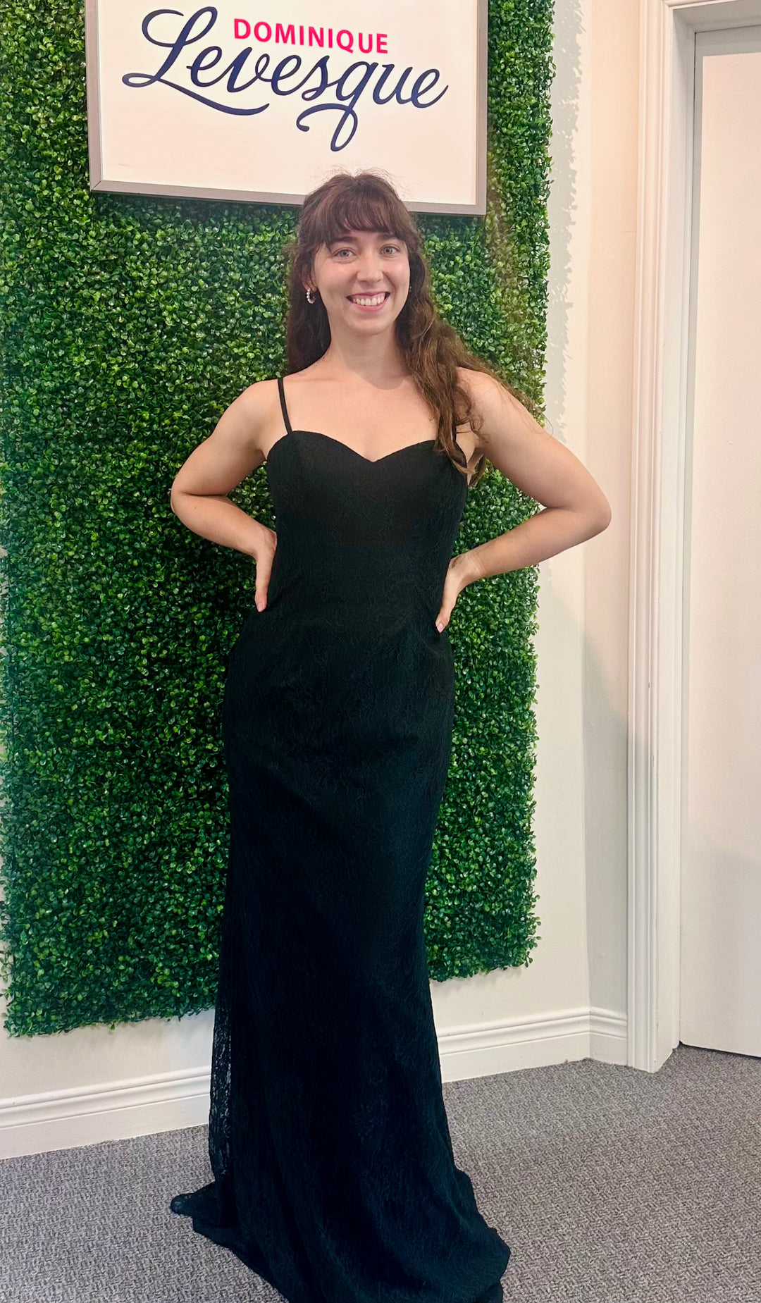 Woman in a black dress standing in front of a green wall with a sign above.