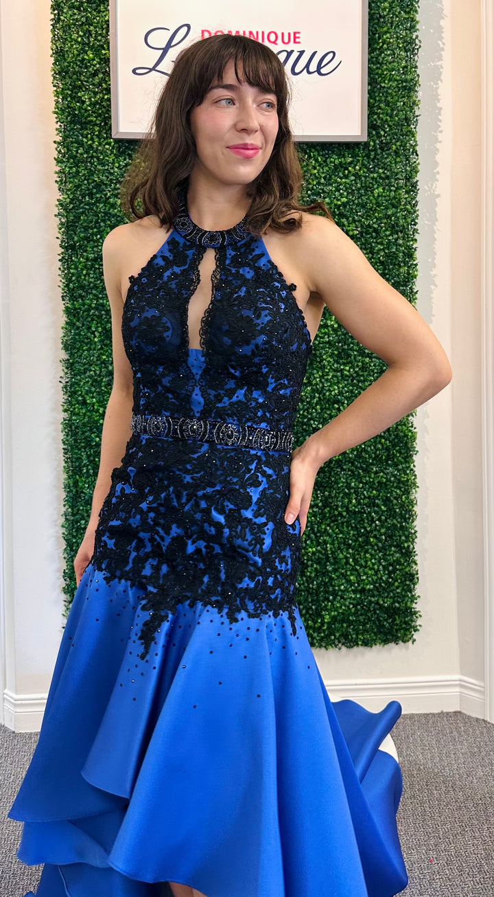 Woman wearing a blue and black dress with a green wall and framed picture in the background