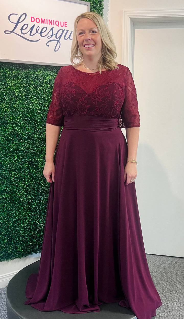 Woman wearing a burgundy evening gown with lace detailing in front of a green wall and white door.