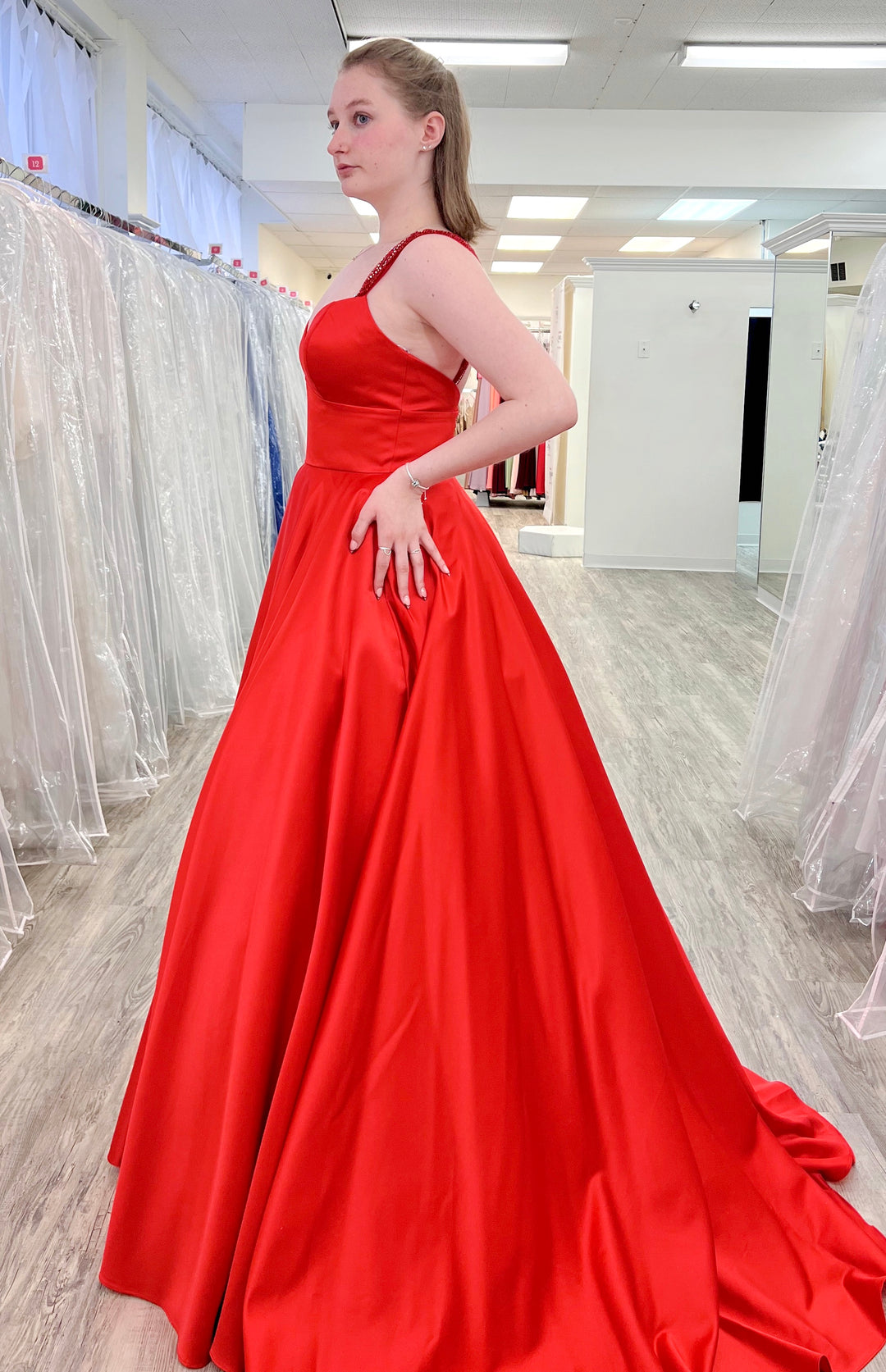 Woman wearing a red evening gown in a fitting room.