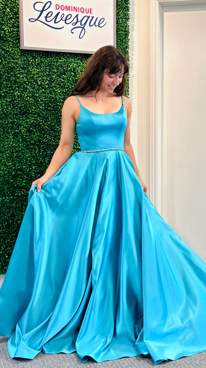 Woman in a blue evening gown standing against a green wall with a sign.