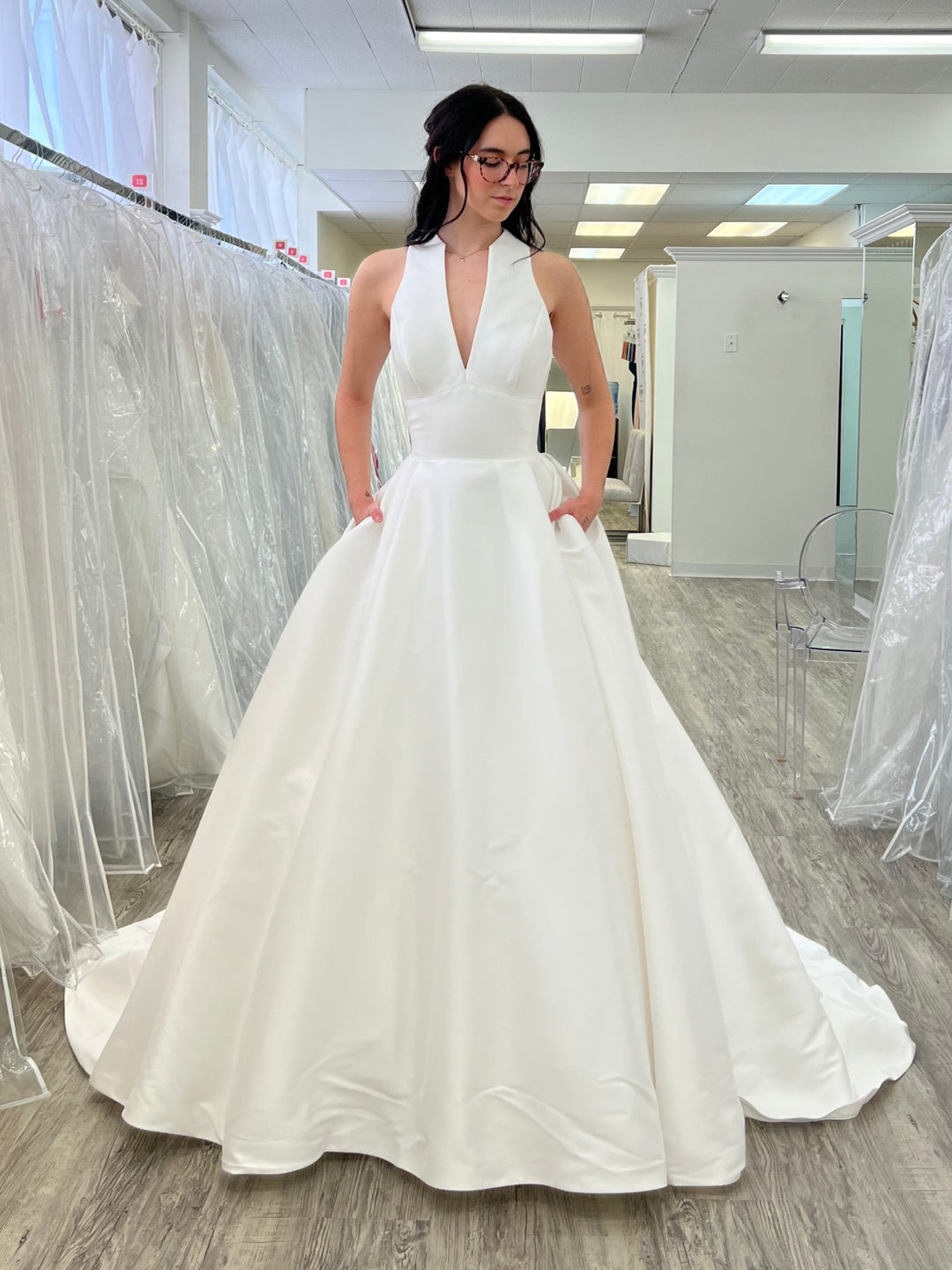 Woman in a white wedding dress standing in a store with multiple wedding dresses on display.