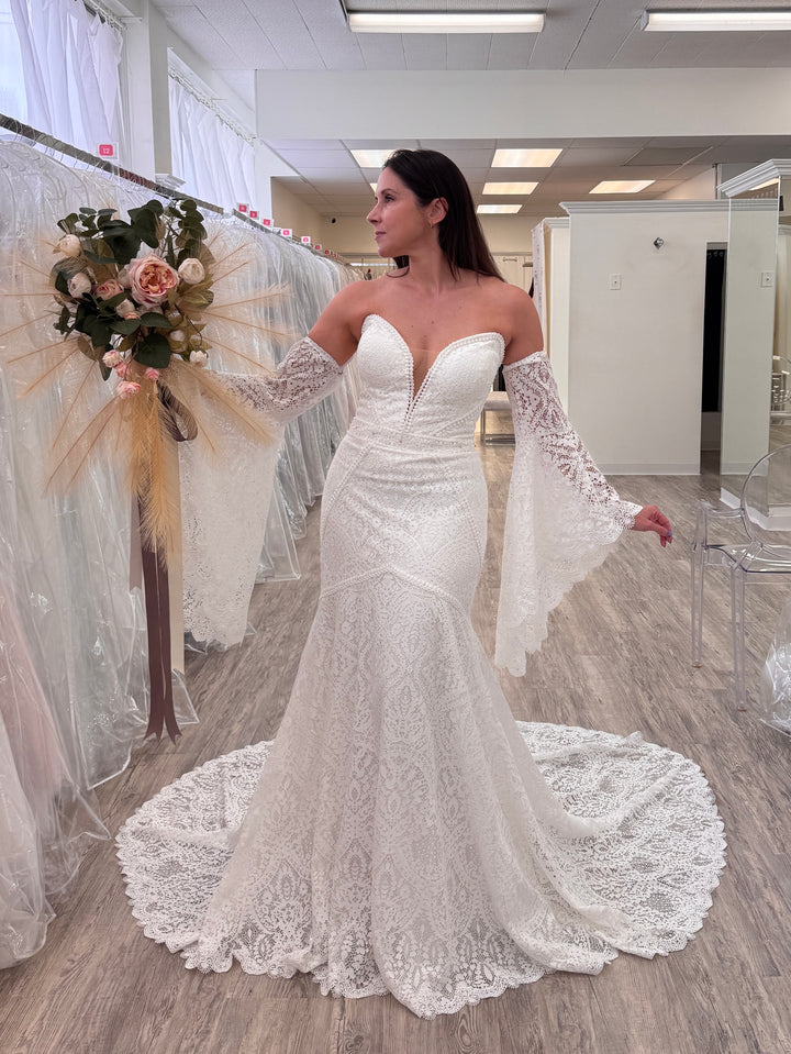 Woman in a white lace wedding dress holding a bouquet in a store.