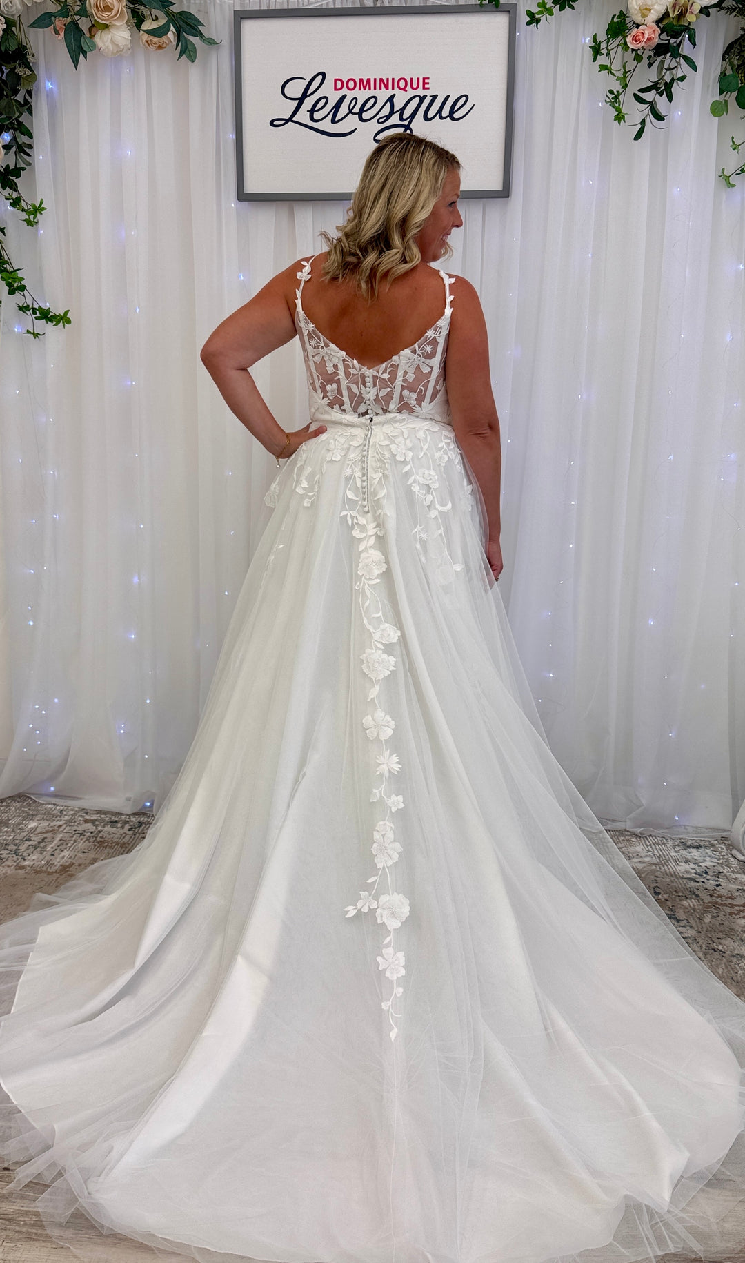 Woman wearing a white wedding dress with floral details in a decorated indoor setting.