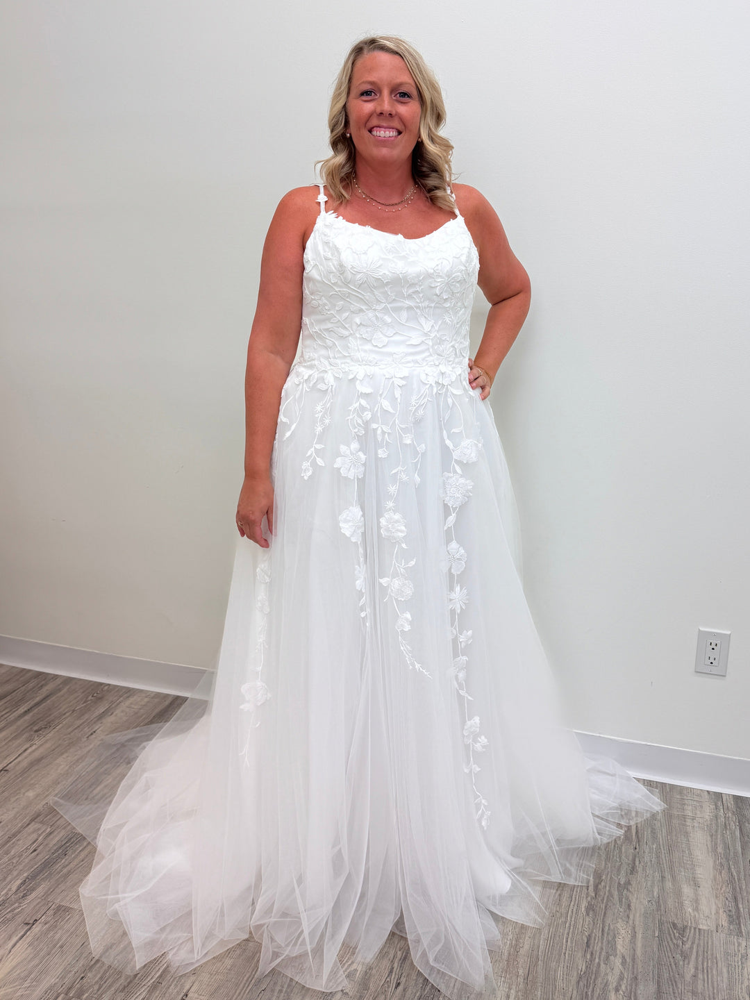 Woman wearing a white wedding dress with floral details in a minimal indoor setting.