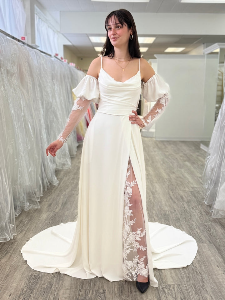 Woman wearing a white wedding dress with floral lace details in a bridal shop.