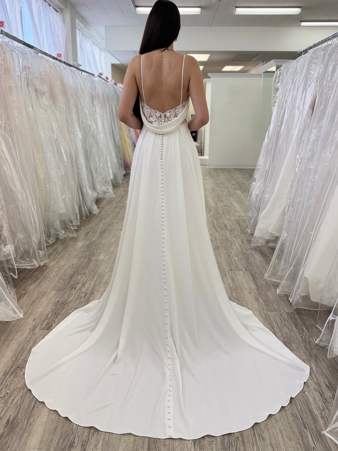 Woman wearing a white wedding dress in a fitting room with mirrors.