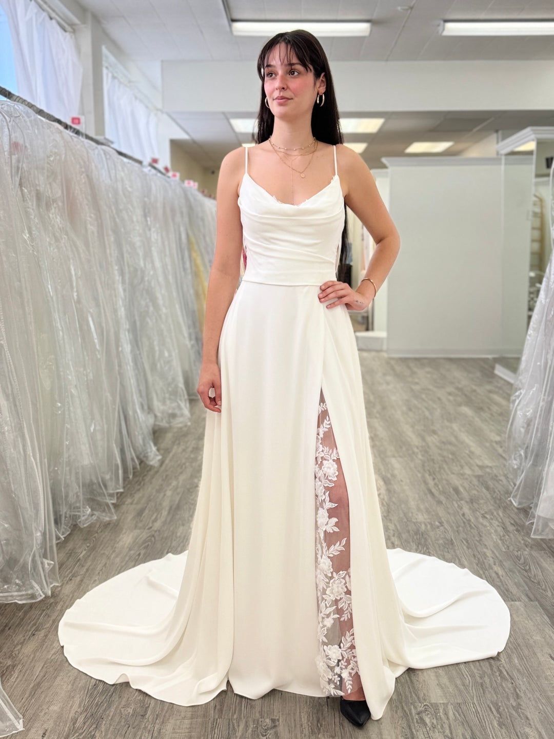 Woman wearing a white wedding dress with lace detailing in a store setting.