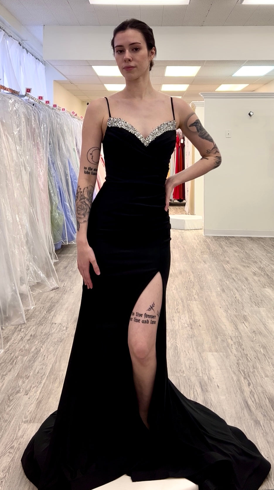 Woman wearing a black evening gown with a slit in a fitting room.