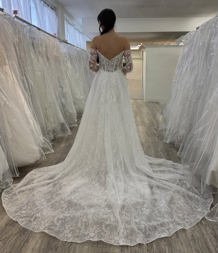 Woman wearing a white lace wedding dress in a fitting room.