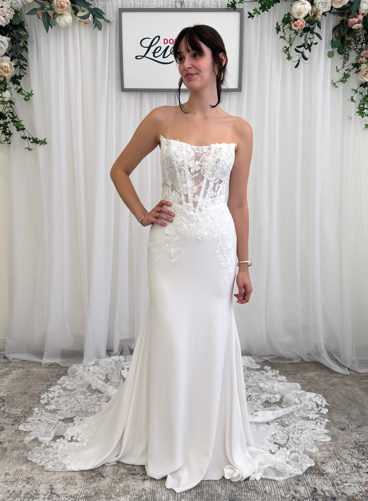 Woman wearing a strapless wedding dress with floral lace details in a decorated room.