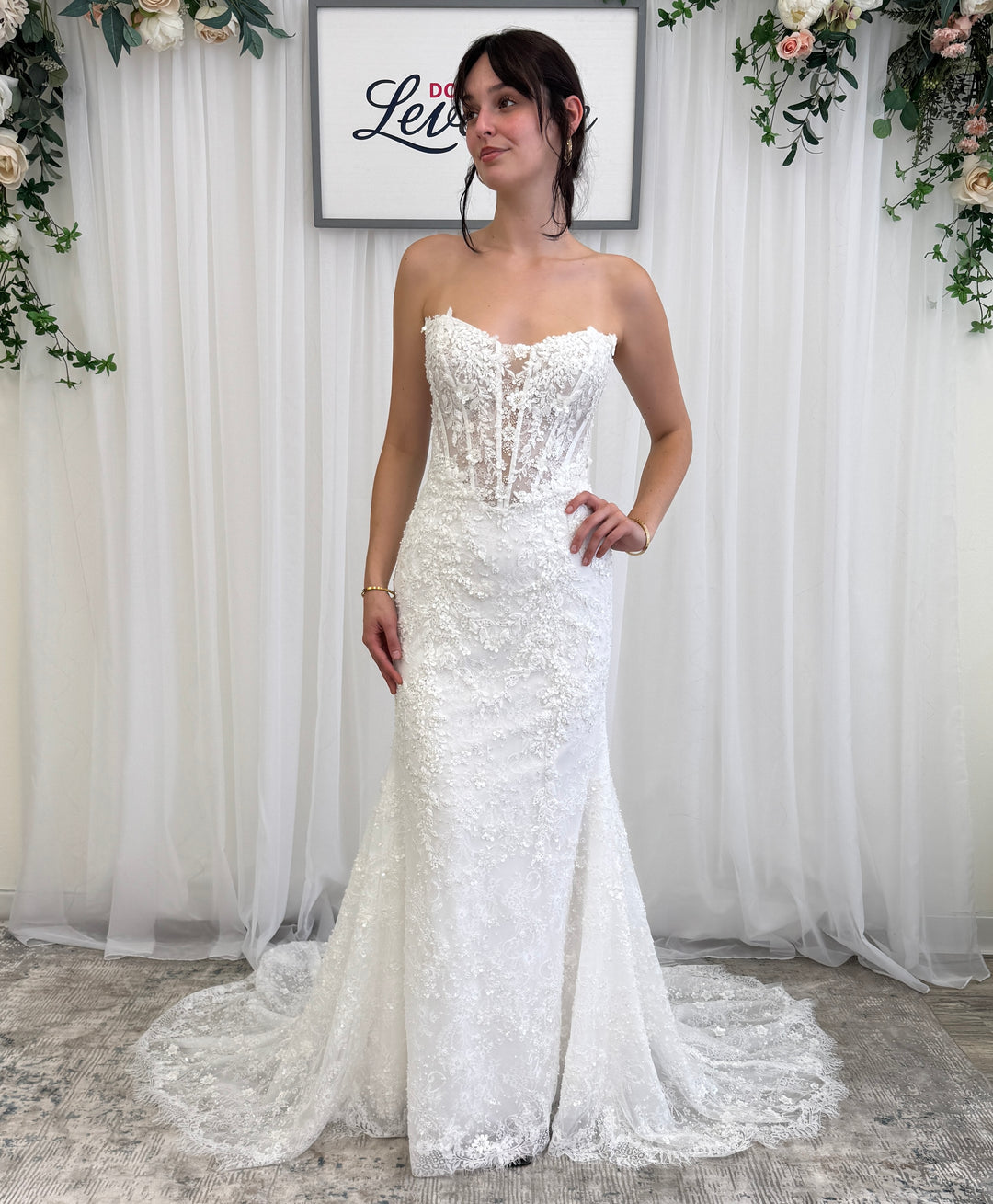 Woman wearing a white lace wedding dress in a decorated room with floral arrangements in Dominique Levesque Bridal Ottawa