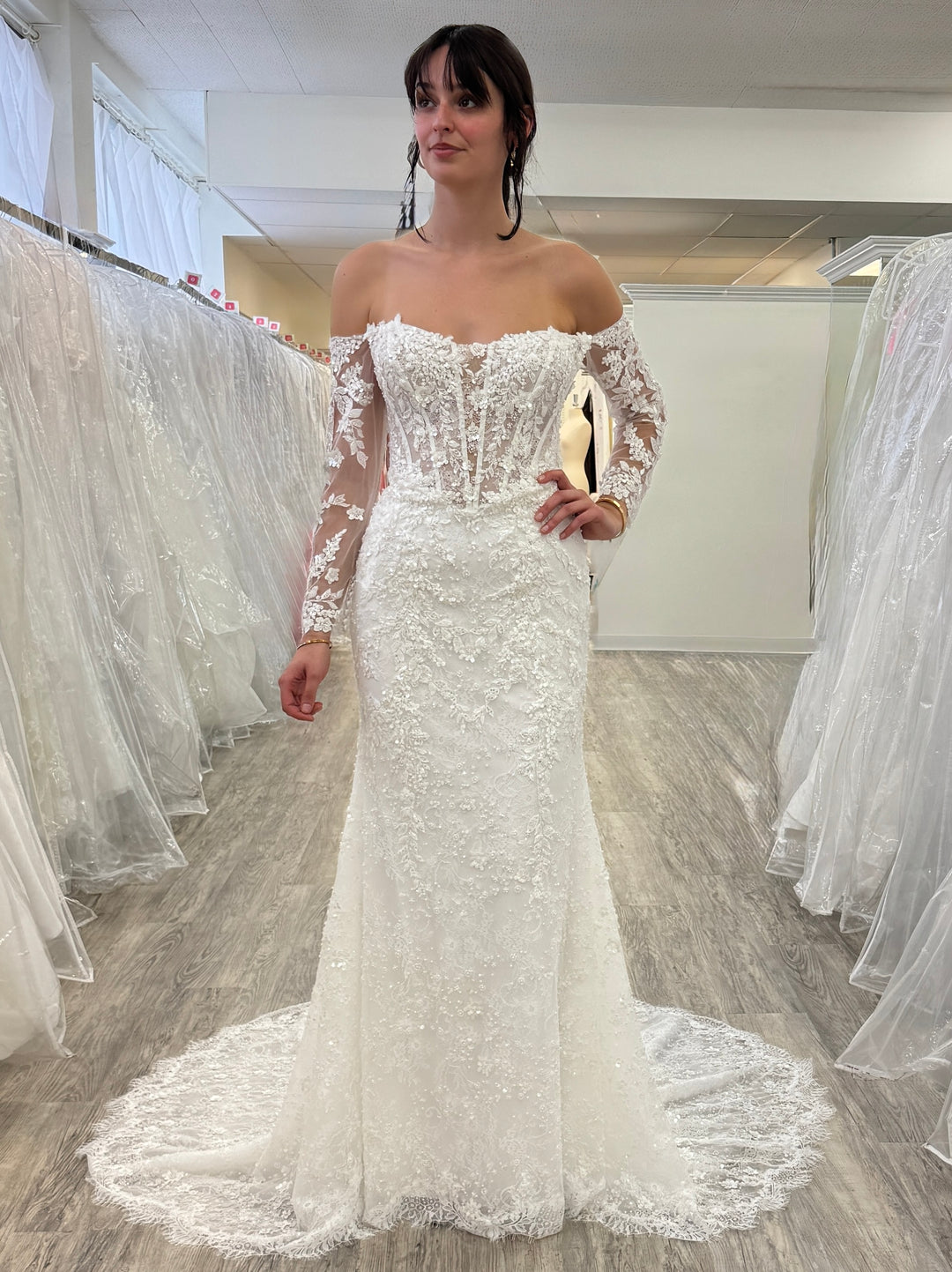 Woman wearing a white lace wedding dress in a fitting room.