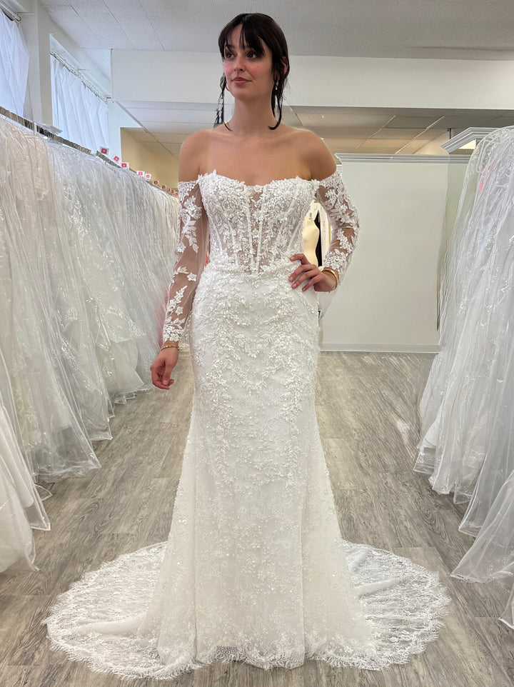 Woman wearing a white lace wedding dress in a fitting room.