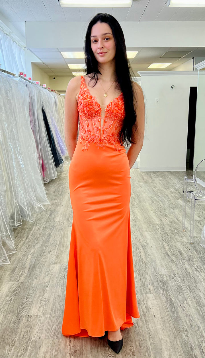 Woman wearing an orange evening gown with lace details in a fitting room.