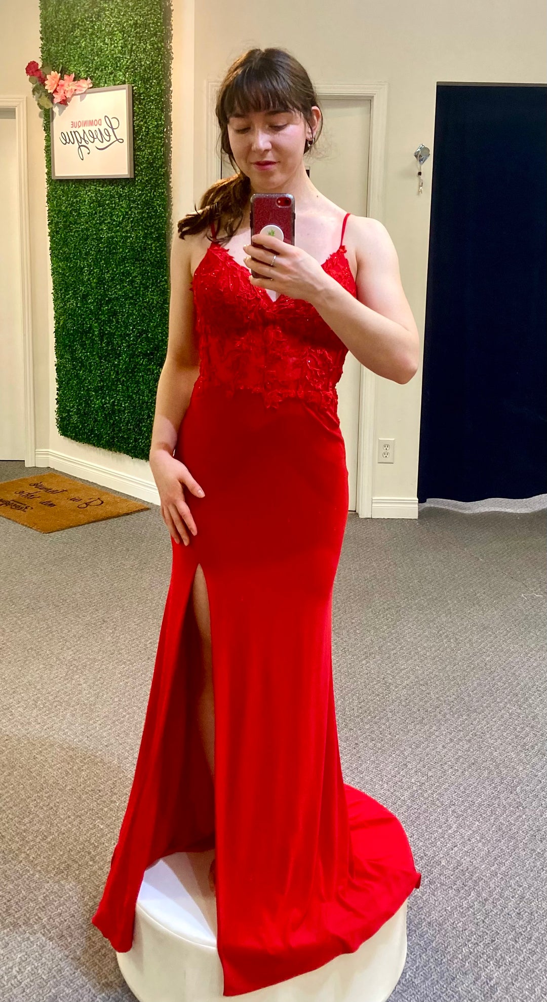 Woman in a red evening gown taking a mirror selfie in a fitting room.