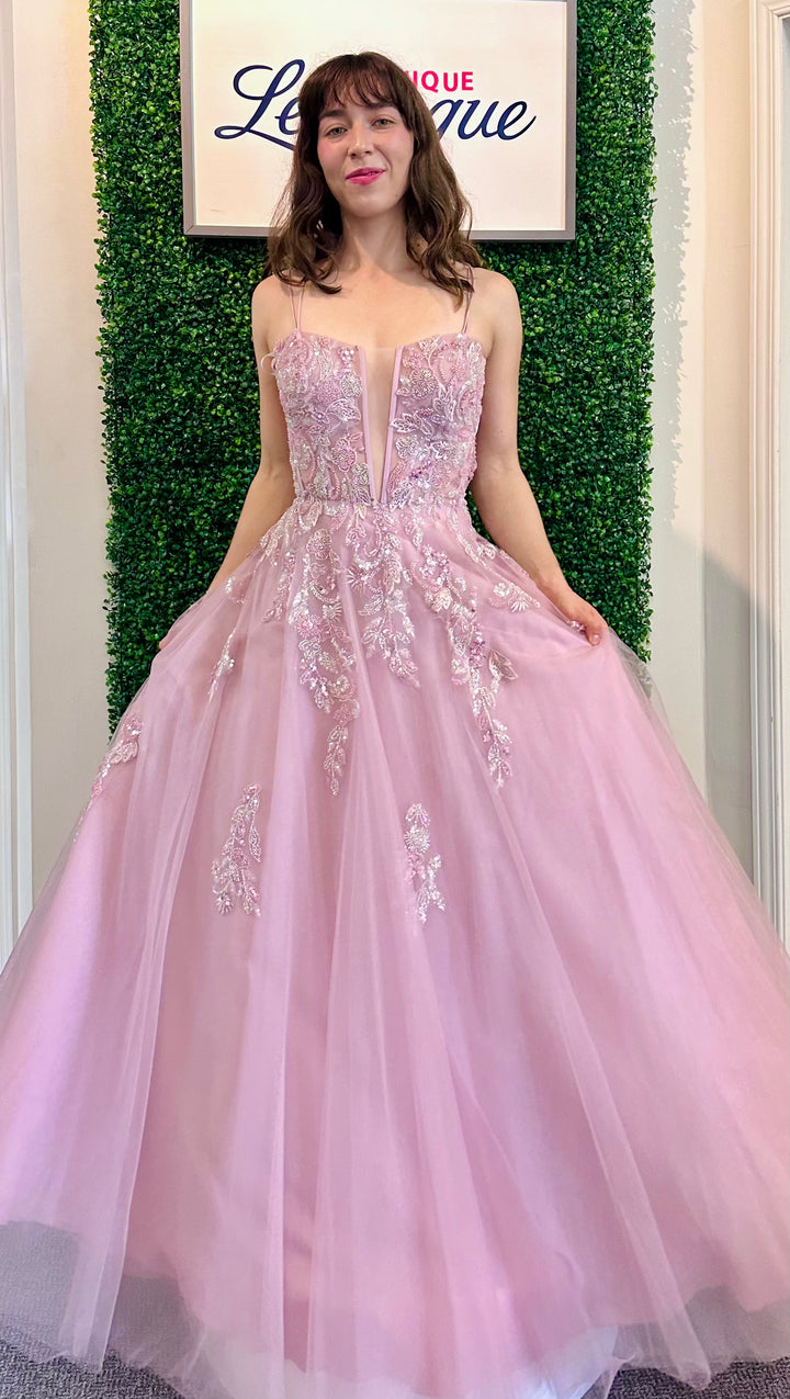 Woman in a dusty rose evening gown with floral details against a green leafy background