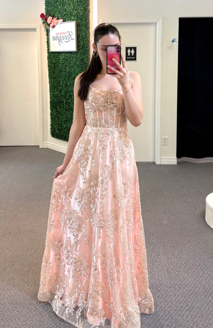 Woman wearing a long, light pink dress with floral details in a room.