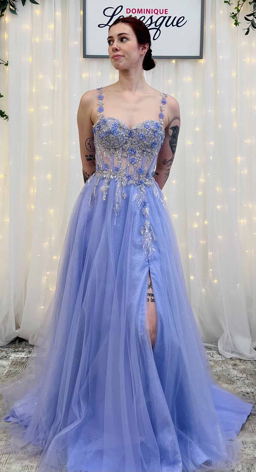 Woman wearing a lavender evening gown with intricate detailing in a softly lit room.