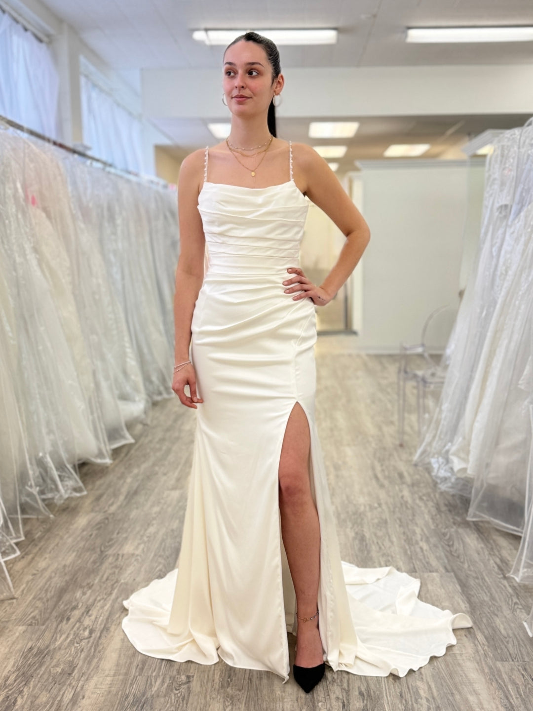 Woman wearing a white wedding dress with a slit in a fitting room.