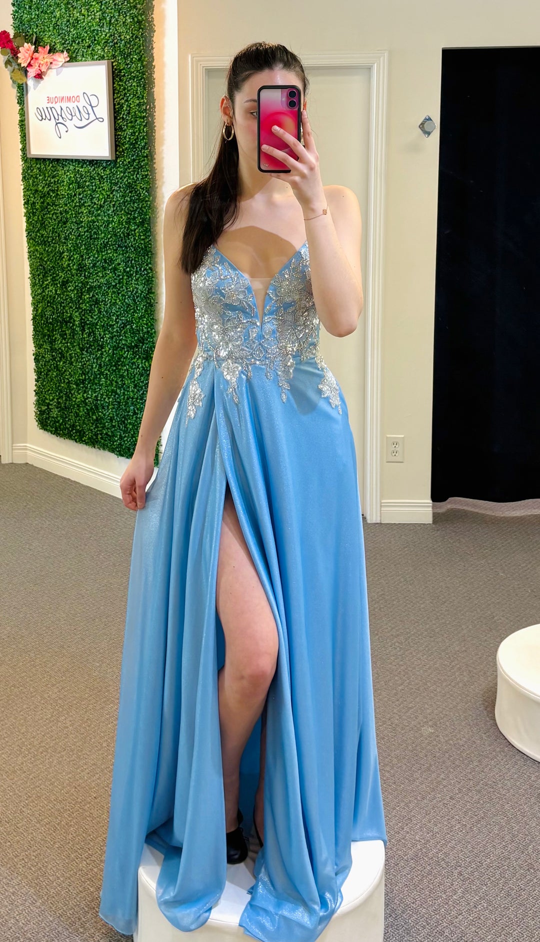 Woman in a blue evening gown with a high slit standing in front of a mirror.