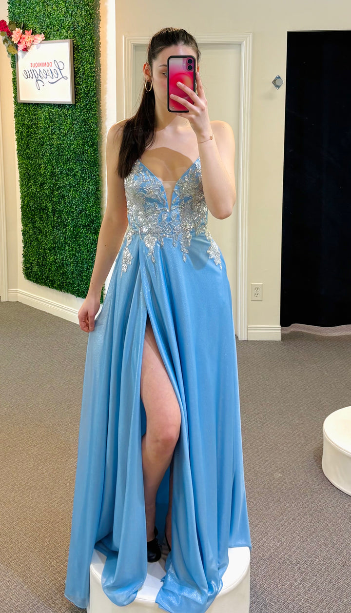 Woman in a blue evening gown with a high slit standing in front of a mirror.