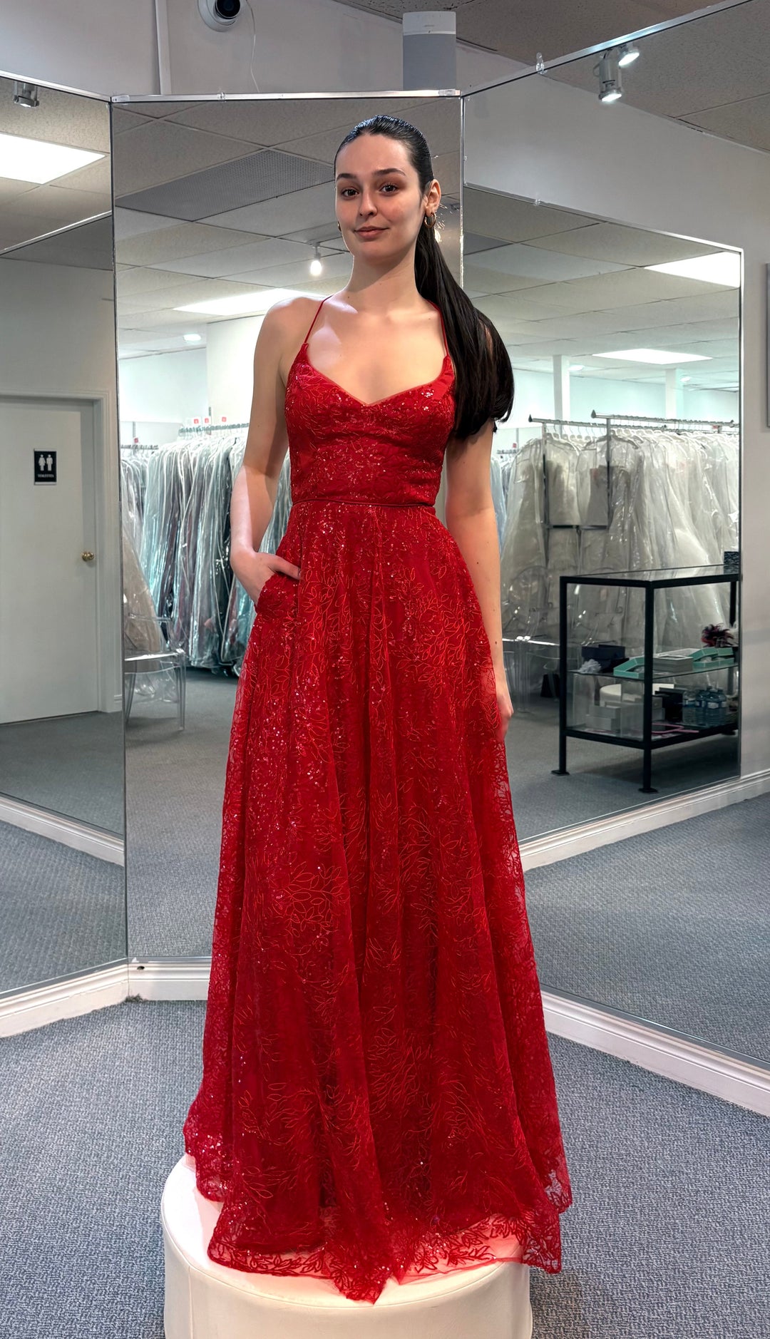 Woman in a red dress standing in front of a mirror in a fitting room.