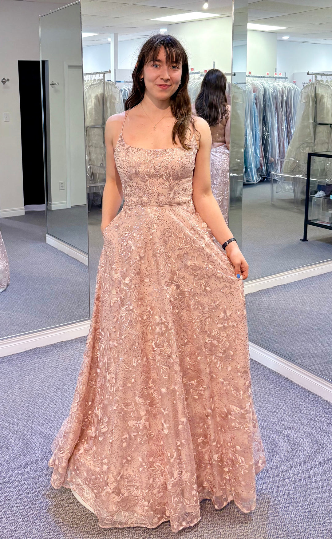 Woman wearing a sparkly pink dress in a fitting room.