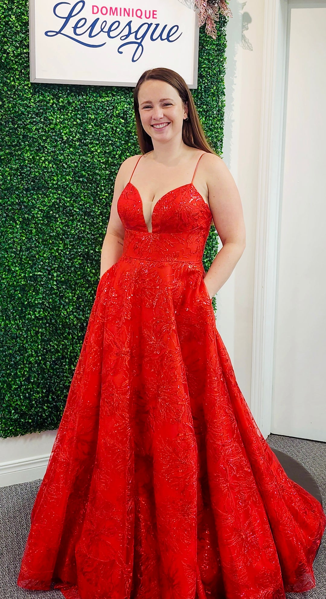 Woman in a red dress standing in front of a green wall with 'Dominique Levesque' branding.
