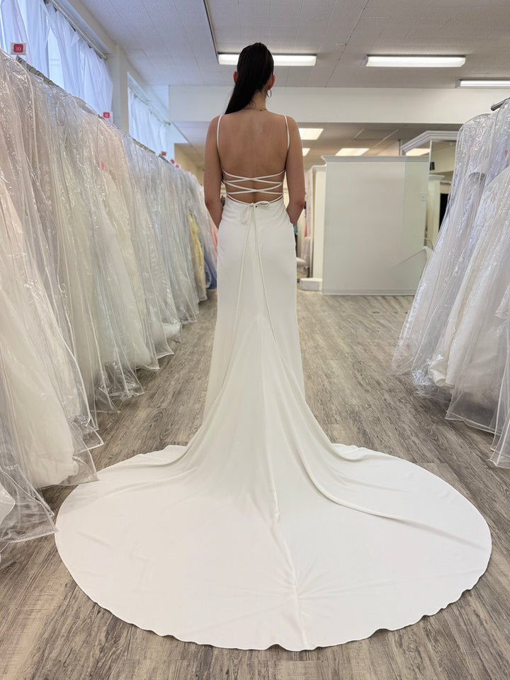 Person wearing a white wedding dress in a fitting room with other dresses around.