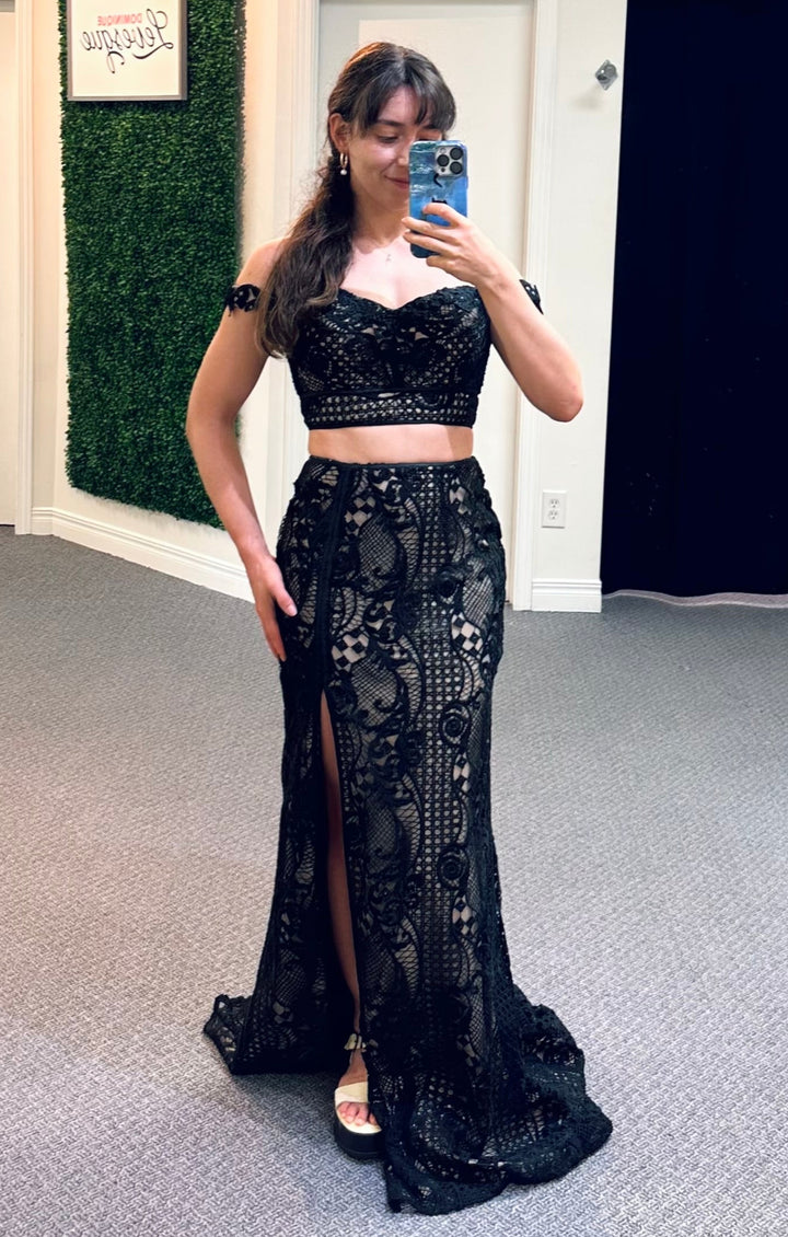 Woman taking a mirror selfie wearing a two piece black lace outfit in a fitting room.
