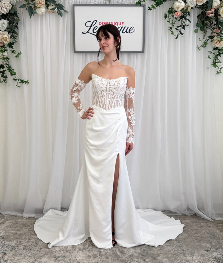 Woman in a white wedding dress with lace sleeves standing in front of a floral backdrop.