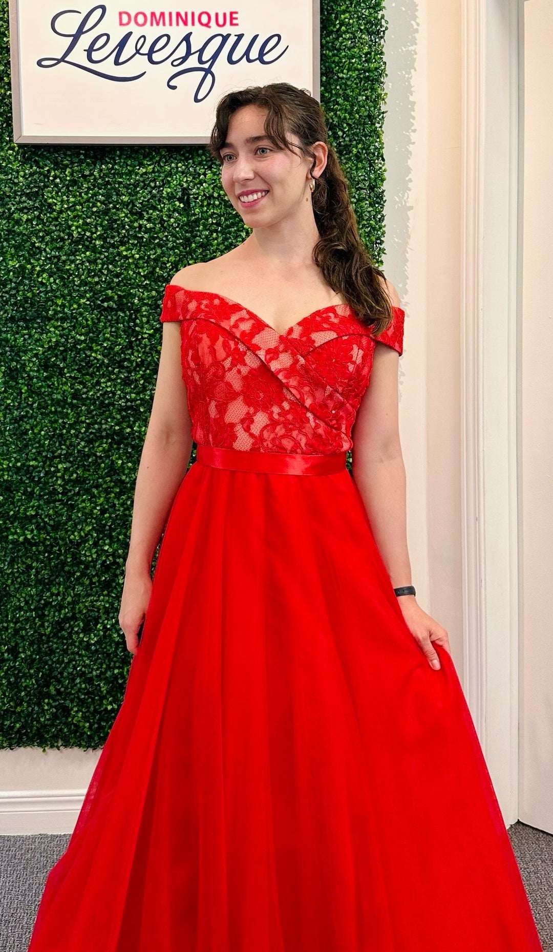 Woman in a red dress standing against a green leafy background with 'Dominique Levesque' branding.
