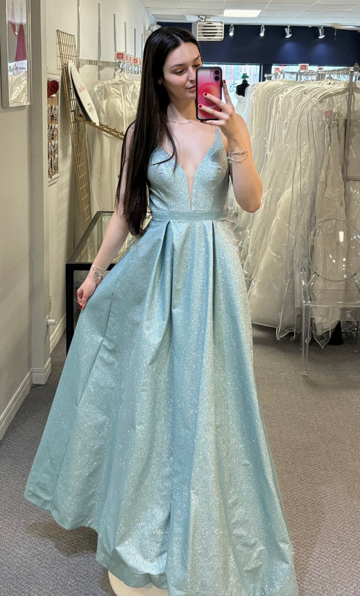 Woman in a light blue evening gown taking a mirror selfie in a fitting room.