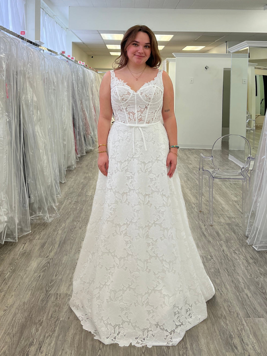 Woman in a white wedding dress standing in a store with multiple wedding dresses displayed.