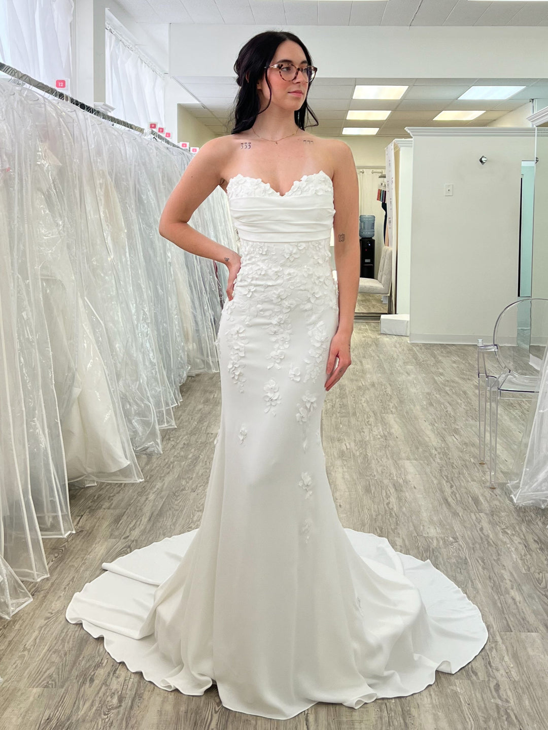 Woman in a white fit and flare wedding dress is standing in a bridal shop with dresses on racks.