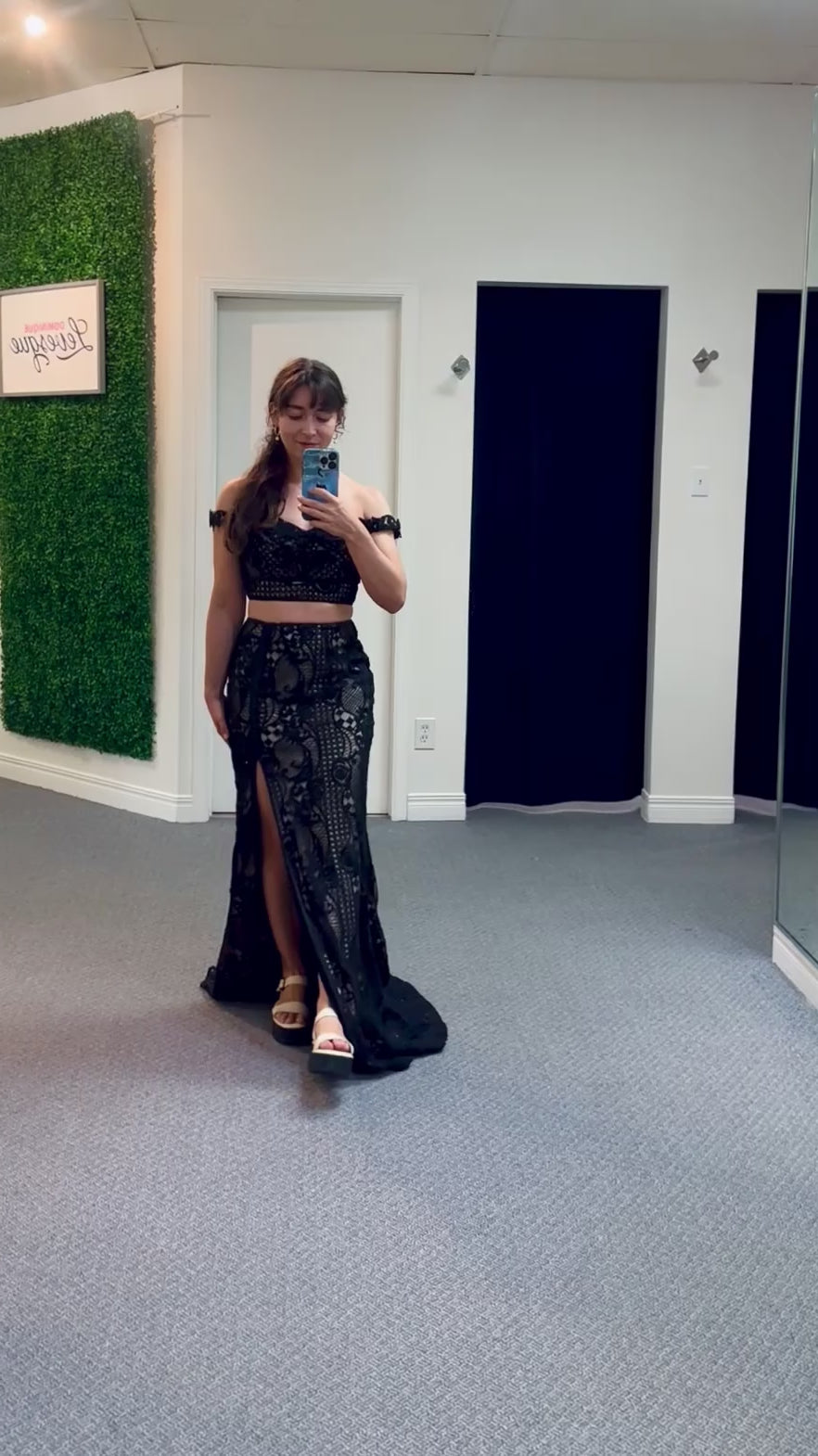 Woman taking a mirror video wearing a two piece black lace outfit in a change room.