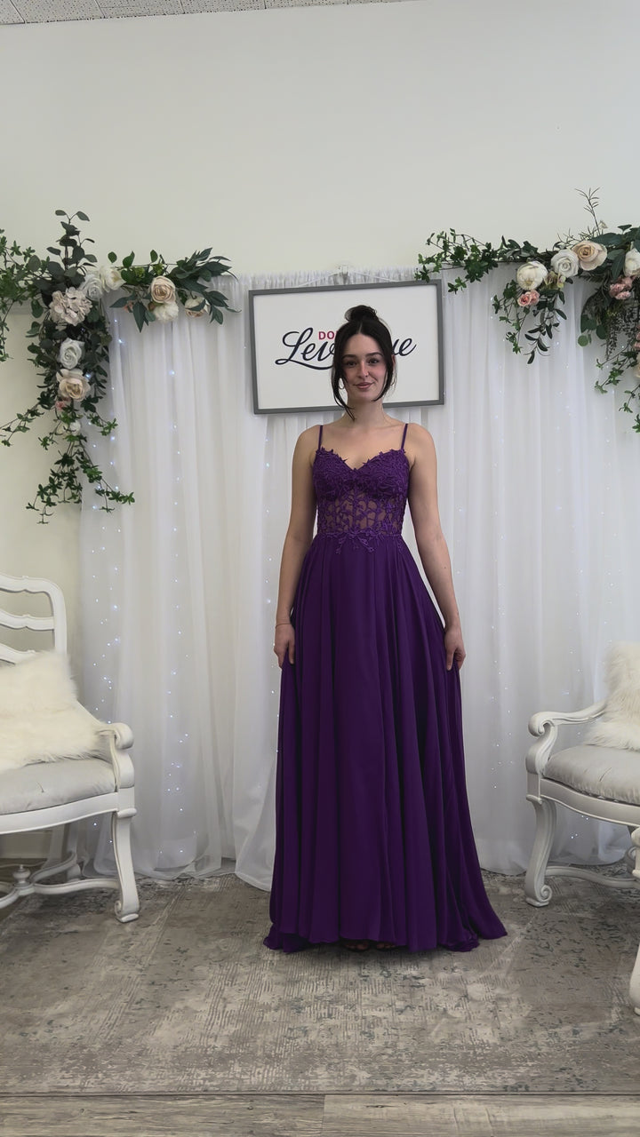 Woman wearing a purple gown in a fitting room with mirrors and dresses.