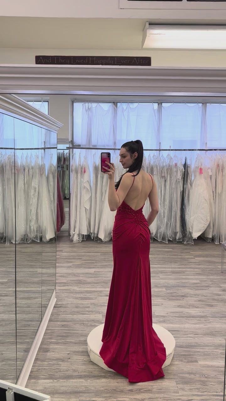 Woman in a red evening gown taking a mirror selfie in a fitting room.