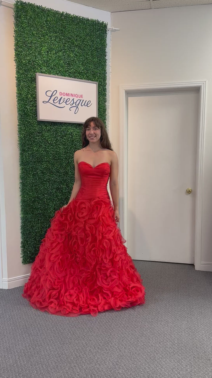 Woman in a red strapless gown standing against a green wall with a sign above.