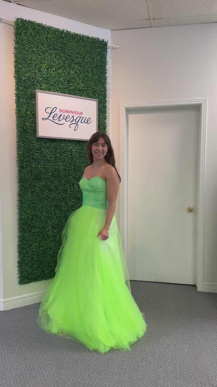 Woman wearing a lime strapless gown in an indoor setting with a green wall.